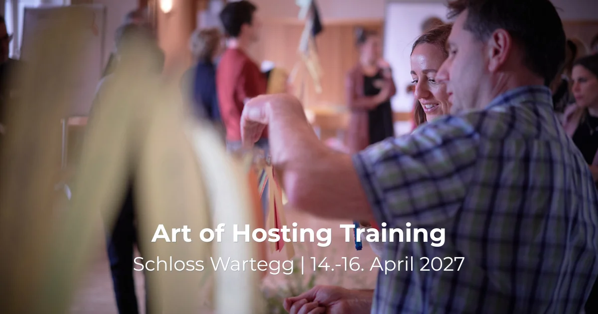 Ein Bild aus dem Art of Hosting Training zeigt im Vordergrund eine Frau und ein Mann, die einen Zettel auf einer Leine aufhängen.
