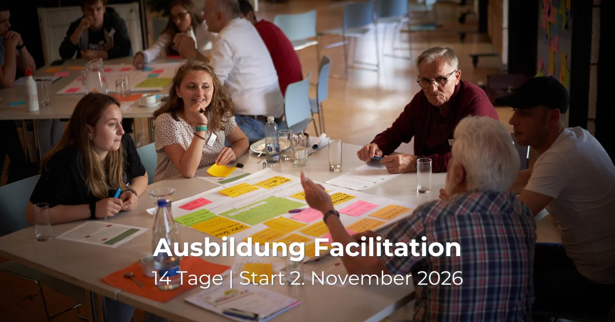 Das Bild zeigt Menschen unterschiedlichen Alters, die um einen Tisch sitzen und sich austauschen und notieren.